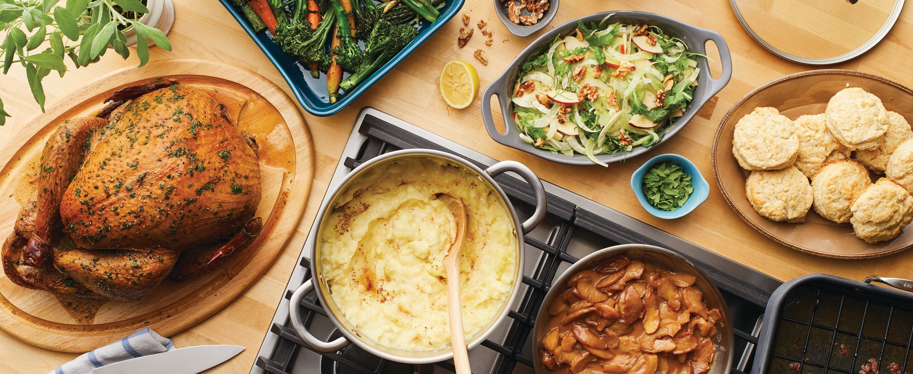 A table set with roast chicken, mashed potatoes, stewed apples, biscuits, a green salad, and a dish of roasted vegetables.