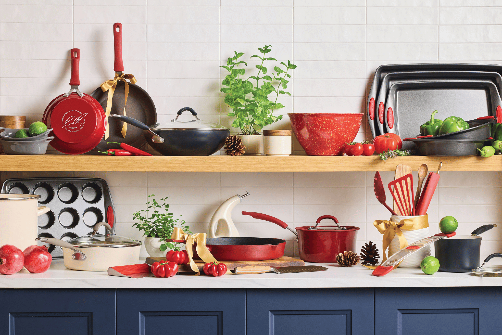 A kitchen counter and shelves display assorted red cookware, utensils, bakeware, vegetables, herbs, and decorative items against a white tile wall.