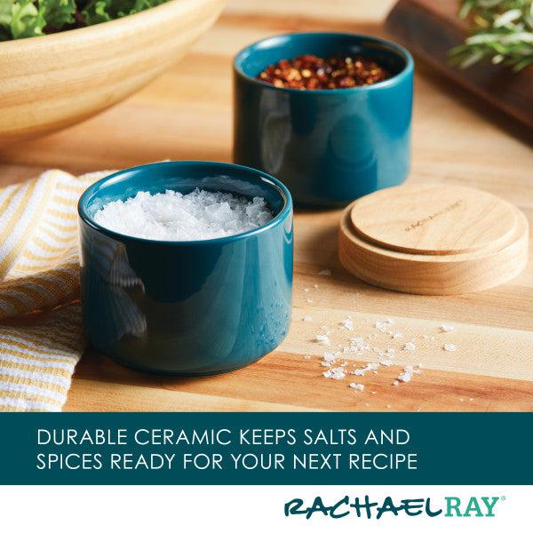 The Stacking Spice Box Set, arranged like elegant ceramic bowls, overflows with an assortment of salts and spices on a wooden surface.