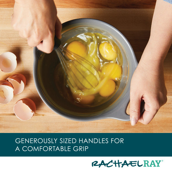 Hands whisking eggs in the 2-Piece Ceramic Mixing Bowl Set next to cracked egg shells on a wooden surface.