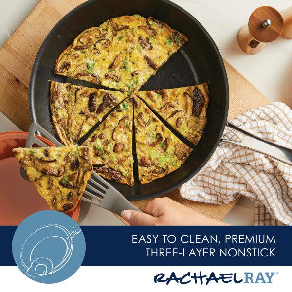 The Cook + Create Hard Anodized Nonstick Frying Pan, featuring a triple-layer nonstick surface, elegantly holds a sliced frittata and comes with a spatula, all resting on a wooden board.