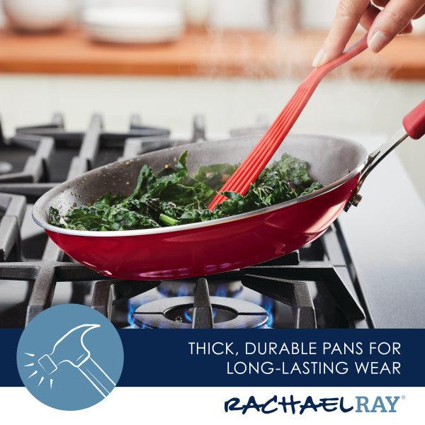 A Cook + Create Nonstick Cookware pan in red is on the stove, complemented by greens and paired with a matching red spatula. This cookware set is not just a favorite among chefs but also features exceptional scratch resistance, ensuring long-lasting durability for every culinary masterpiece.