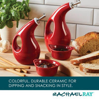 The EVOO Bottle and Ramekin Dipper Set features red ceramic oil dispensers and bowls, ideal for serving bread and herbs, gracefully arranged on a wooden surface. These dishwasher-safe pieces come with an EVOO bottle to ensure your olive oil stays fresh.