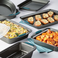 A diverse selection of oven-safe, nonstick baking pans from the 10-Piece Nonstick Bakeware Set with food arranged on a white surface.