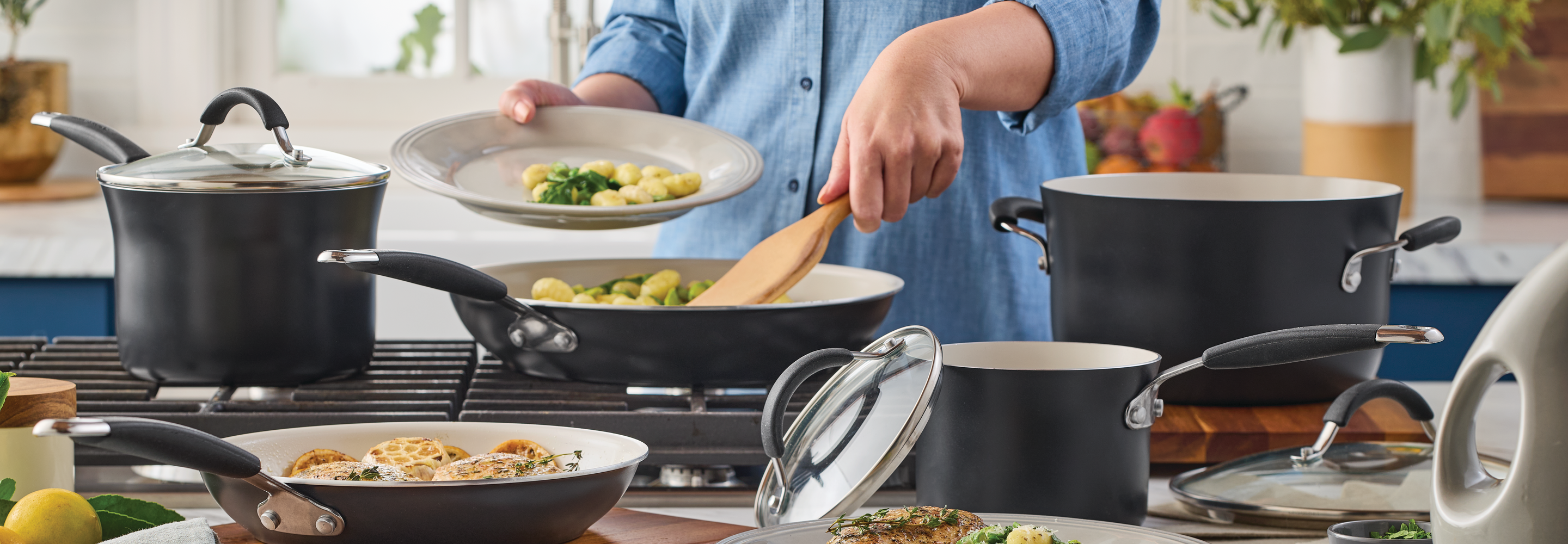 A person using a wooden spatula to cook a meal in a grey Peppercorn-colored 10-piece cookware set on a stovetop.