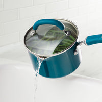 A blue pot pouring water from cooked vegetables into a sink.