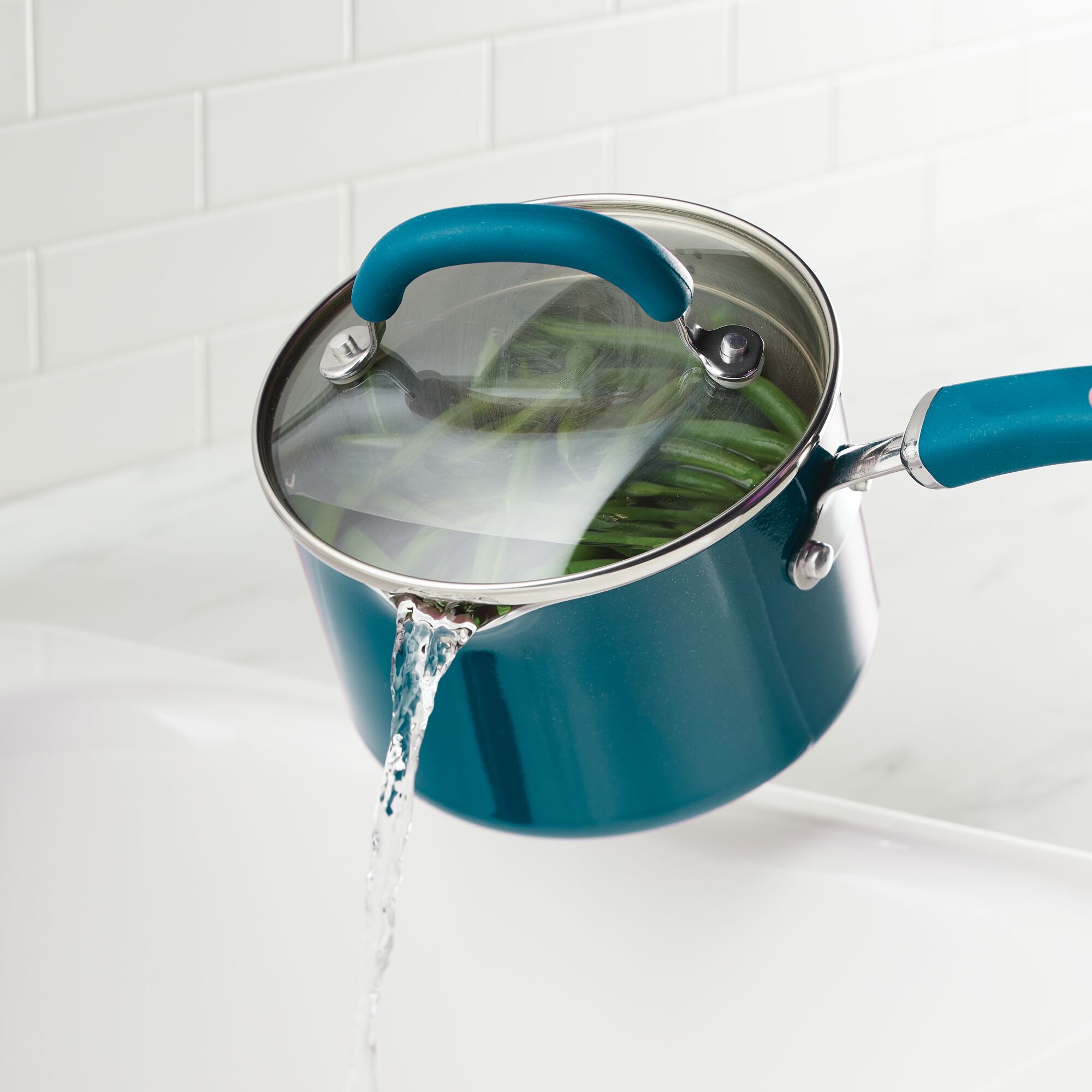 A blue pot pouring water from cooked vegetables into a sink.