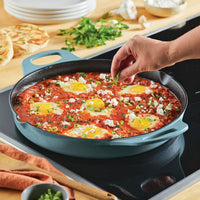 With the 14-Inch NITRO Cast Iron Skillet, someone is expertly seasoning eggs in tomato sauce on a stove. This induction-ready skillet ensures even cooking, and its oven-safe design allows for a seamless transition from stovetop to oven for perfect results.