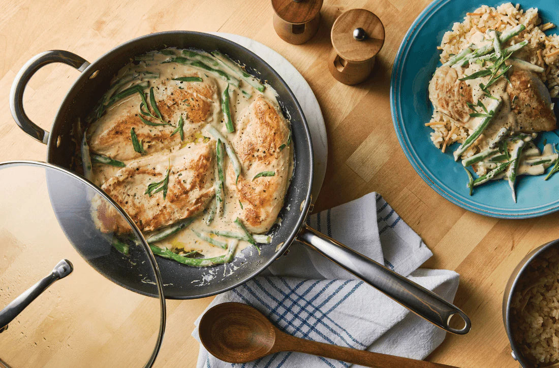 Creamy Dijon-tarragon chicken and green beans served in a 4-quart Rachael Ray Professional Hard Anodized Saucier, served alongside a plate of rice pilaf on a wooden table.