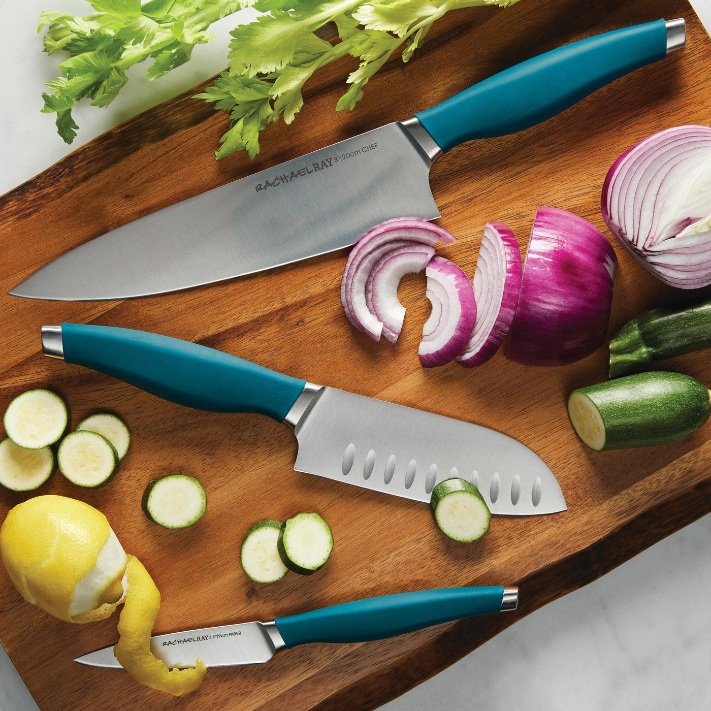 Three knives and sliced vegetables on a wooden board.