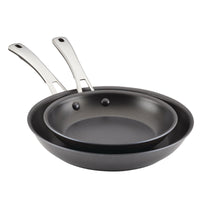 The two frying pans from the 2-Piece Cook + Create Hard Anodized Nonstick Frying Pan Set are stacked neatly, showcasing their gleaming stainless steel handles.