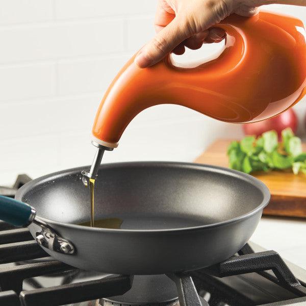 Pouring oil with precision from a 24-ounce EVOO bottle, the translucent stream glides effortlessly through a stainless steel pour spout into the frying pan on the stove.