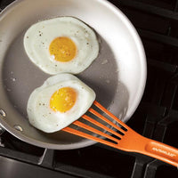 Two fried eggs in a pan with an orange spatula from the 10-Inch & 12-Inch Nylon Spatula Set.