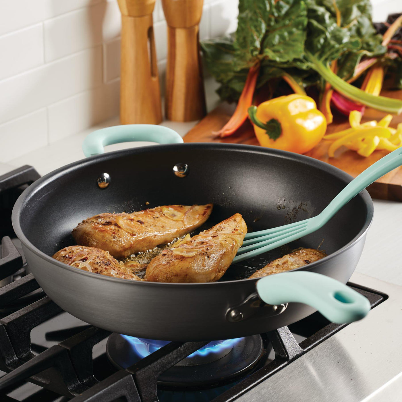 Chicken breasts and veggies cooking in a 12.5" nonstick deep frying pan on the stove.