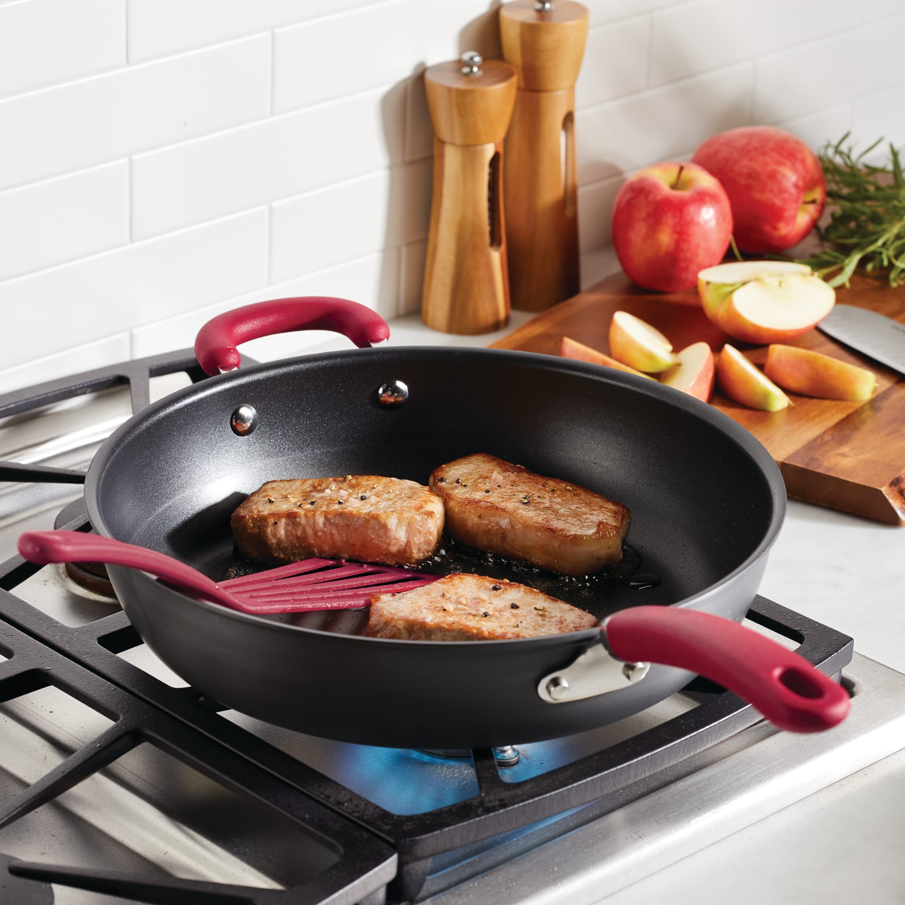 Three pork chops in a 12.5" nonstick pan with apples on the side.